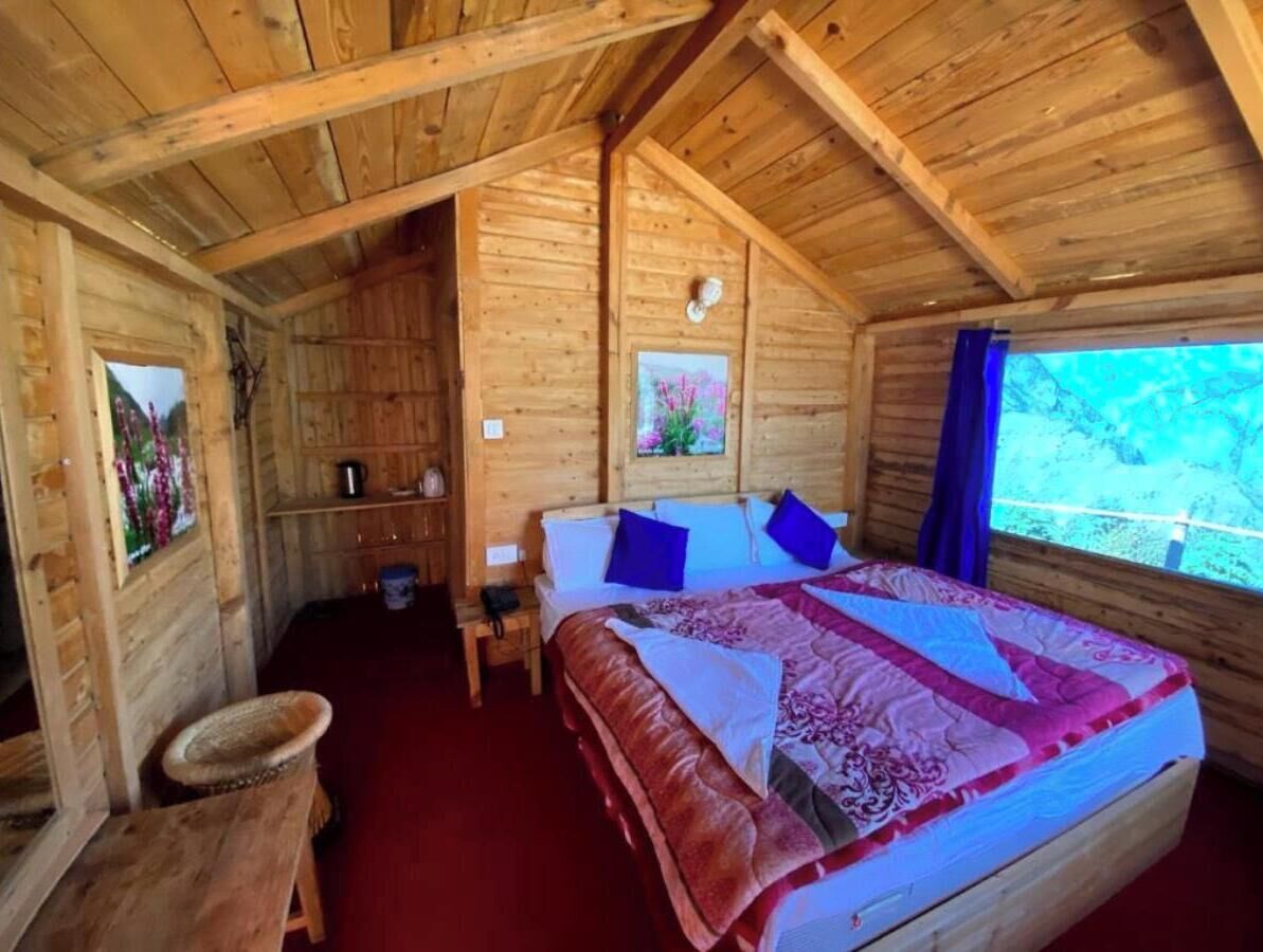Quarto de cabana de madeira com cama, uma mesa pequena, uma cadeira e uma janela com vista para árvores.