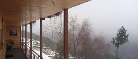 A wooden balcony with a view of a snowy landscape and trees.