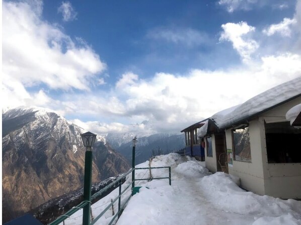 A snow-covered mountain view with a small building and a green railing. - Bluepoppy Resort Auli (Joshimath)