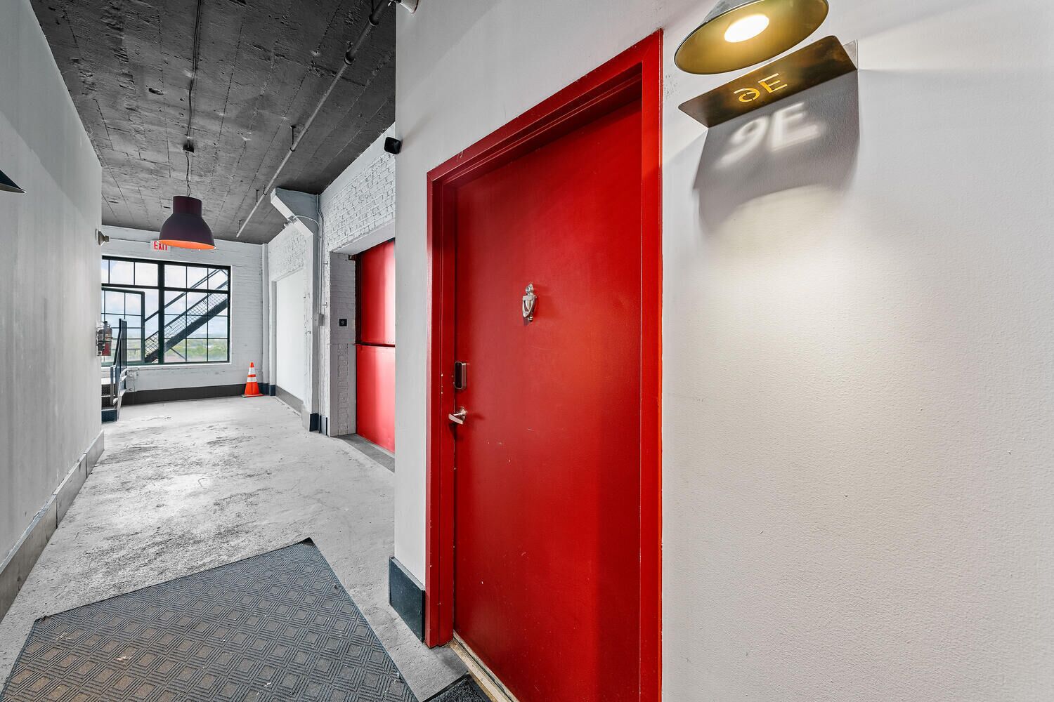 A hallway with a red door, a staircase, and a view of the outdoors.
