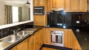 Une cuisine moderne avec des meubles en bois, un évier en acier inoxydable, un four à micro-ondes, un four traditionnel et un réfrigérateur noir.