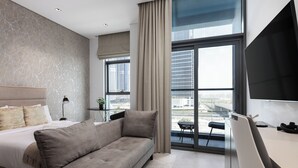 Een moderne hotelkamer met een groot bed, een slaapbank, een bureau en uitzicht op de stad door grote ramen.