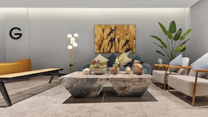 Een moderne woonkamer met een marmeren bijzettafeltje, een bank, een lange houten bank en een grote plant.