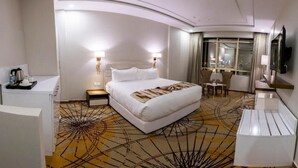 Una habitación de hotel moderna con una cama grande, mesitas de noche, un escritorio, una silla y un televisor.