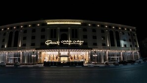 Un hotel grande e iluminado, con una entrada imponente y varias banderas.