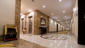 Un pasillo de hotel con piso de mármol, ascensores, una recepción y un revestimiento decorativo.