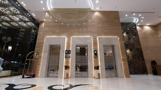 Un moderno vestíbulo de hotel con suelo de mármol, una amplia recepción y una pared decorativa con motivo geométrico.