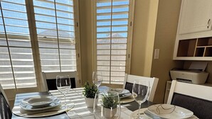 A dining table set with plates, glasses, and a knife, with a view of the outside through large windows.