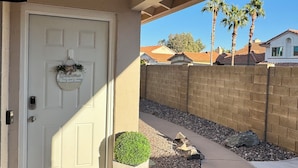 A residential entrance with a white door, a welcome mat, a potted plant, and a clear view of the neighborhood.