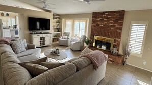 A living room with a sectional sofa, a flat-screen TV, a fireplace, and ceiling fans.