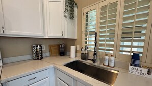 A kitchen with white cabinets, a sink, and a window with blinds.