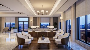 A spacious living area with a central coffee table, multiple seating options, and large windows offering a city view. - By otel Nilüfer  (Bursa)