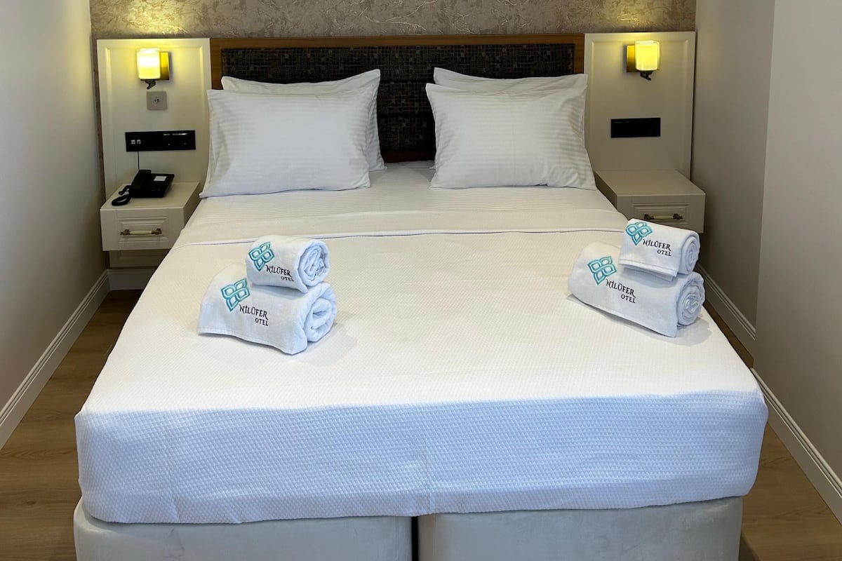 A hotel room with a large bed, two bedside tables, a headboard, and two wall-mounted lamps.