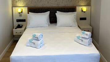 A hotel room with a large bed, two bedside tables, a headboard, and two wall-mounted lamps.