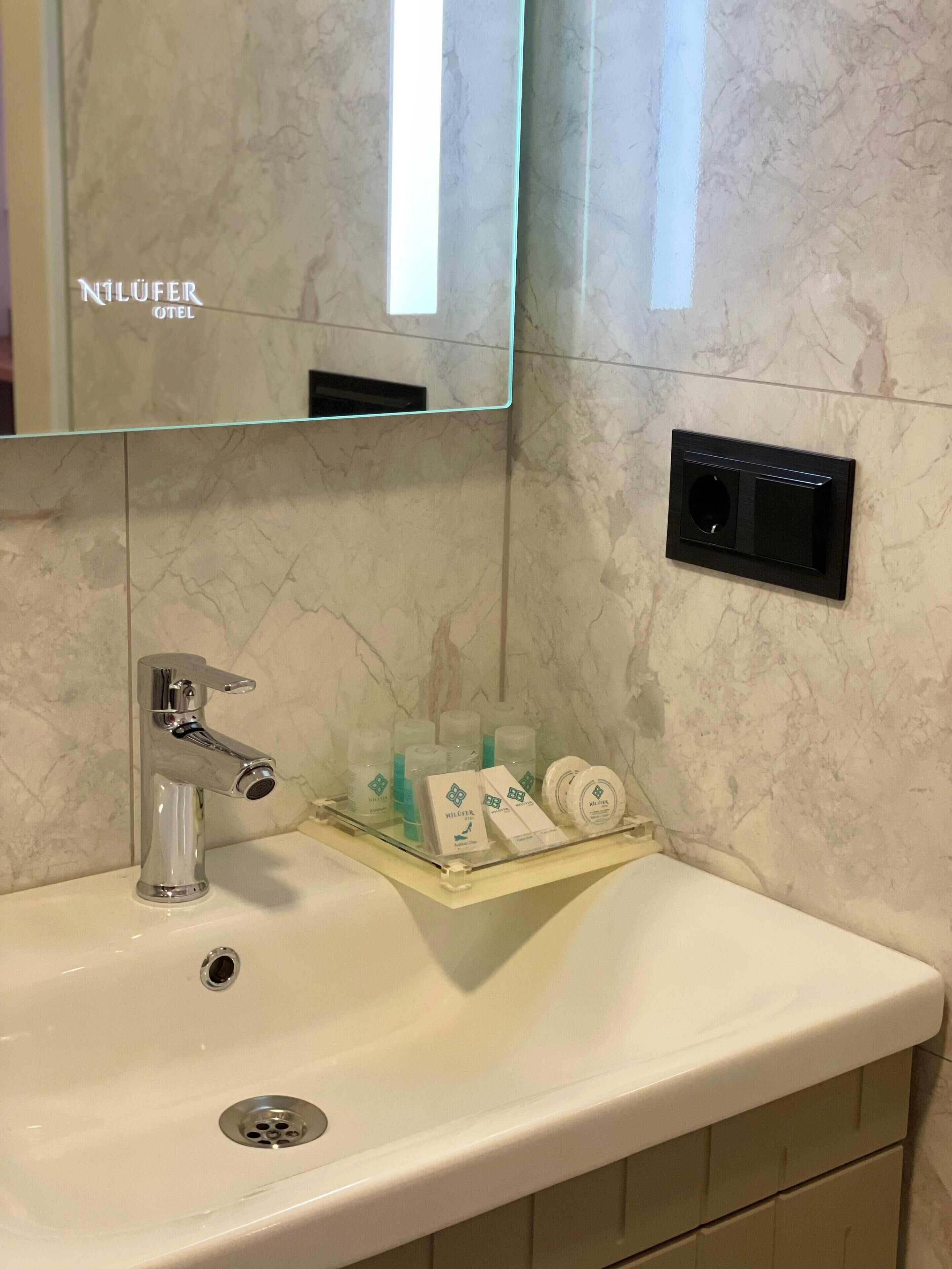 Ein Badezimmer mit Marmorwand, einem Waschbecken mit modernem Wasserhahn und einem Spiegel darüber.