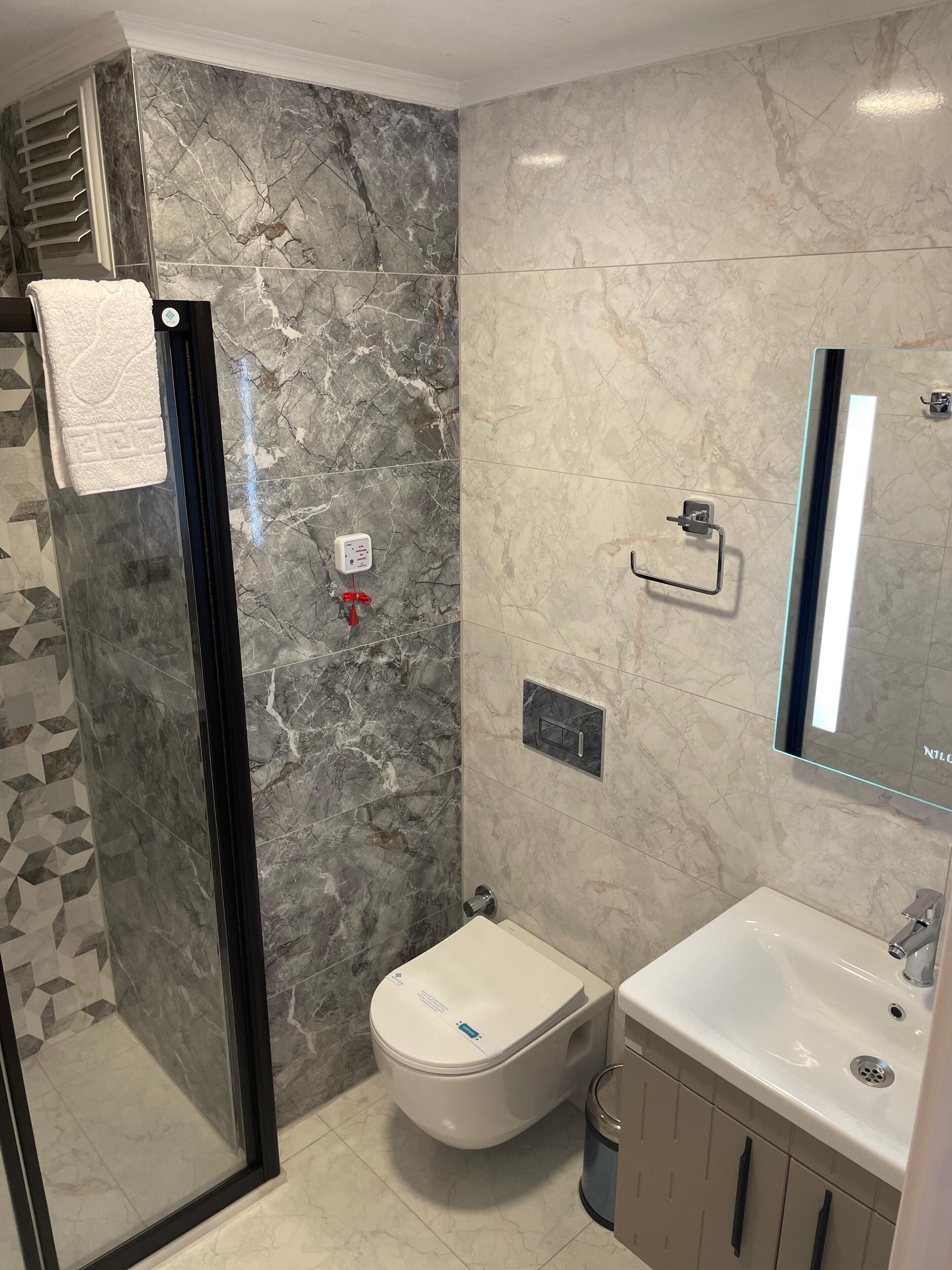 Un baño moderno con cabina de ducha de vidrio, inodoro, lavabo y espejo.