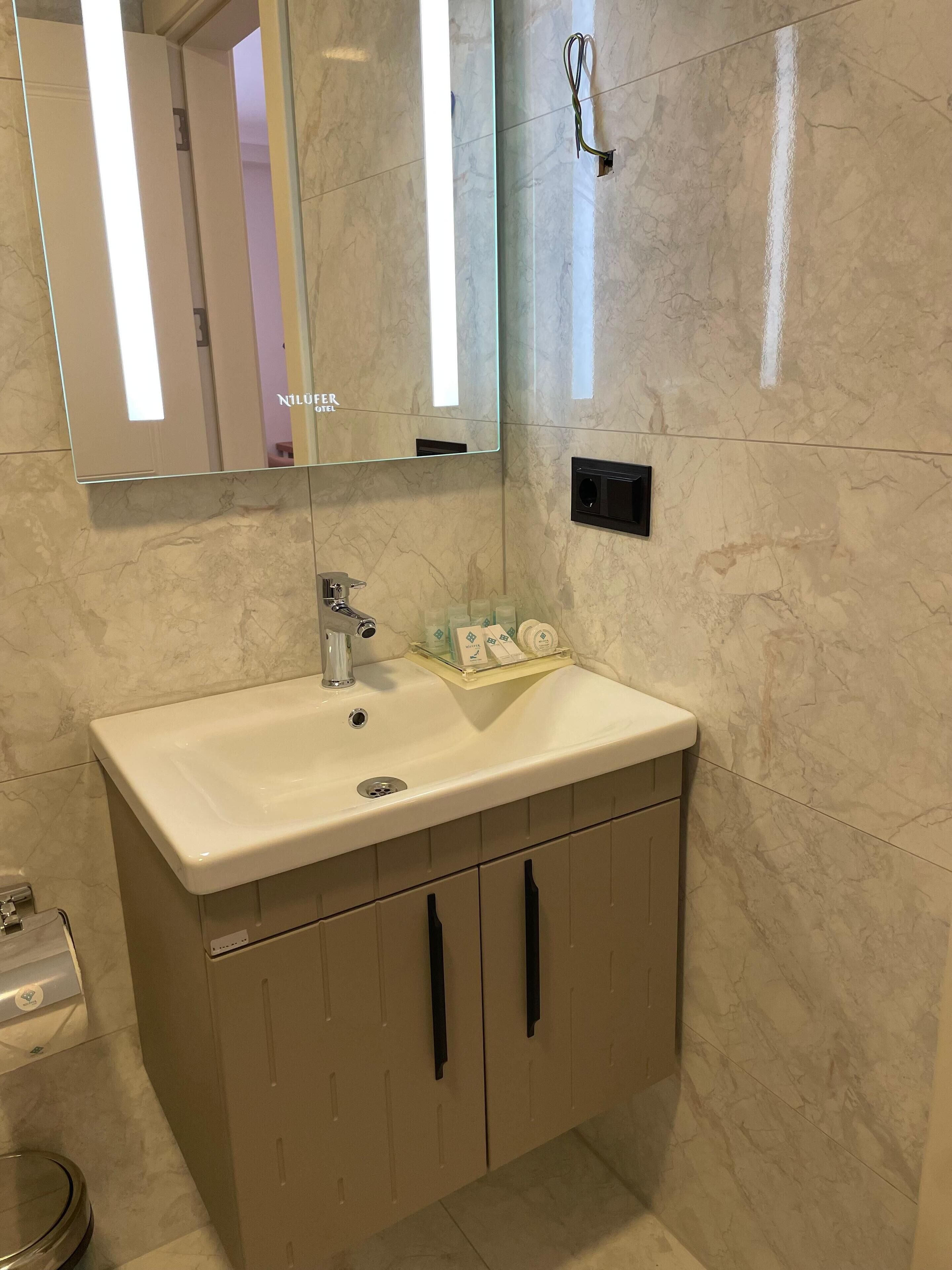 Un baño con lavamanos de mármol, un espejo y un inodoro.