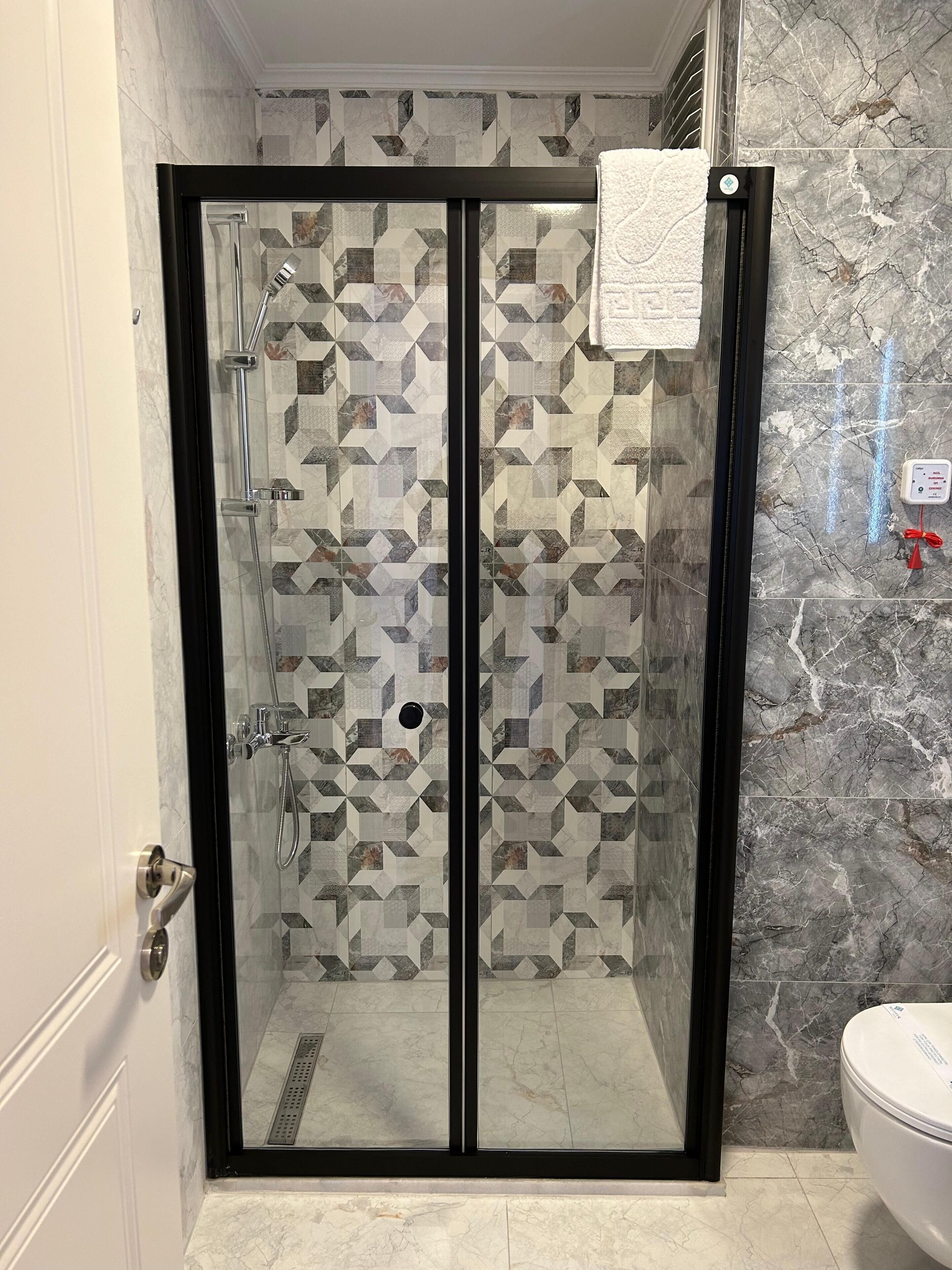 A glass-enclosed shower with a geometric tile backsplash and a marble-patterned wall.