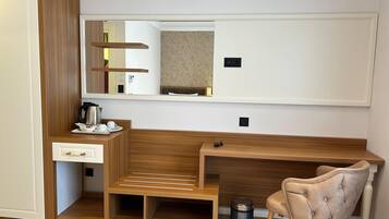 A compact hotel room with a wooden desk, a small seating area, a mirror, and a trash bin.