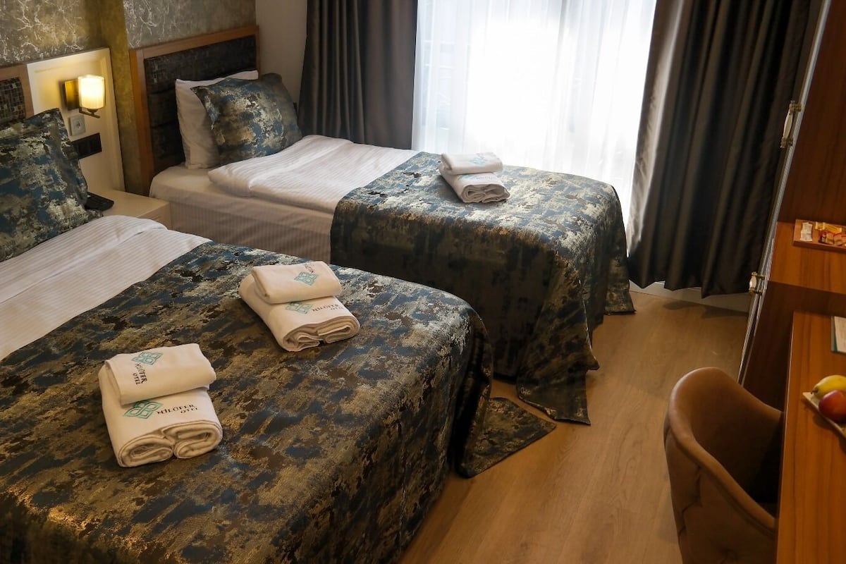 A hotel room with two beds, each with a textured bedspread and a folded towel on the bed.