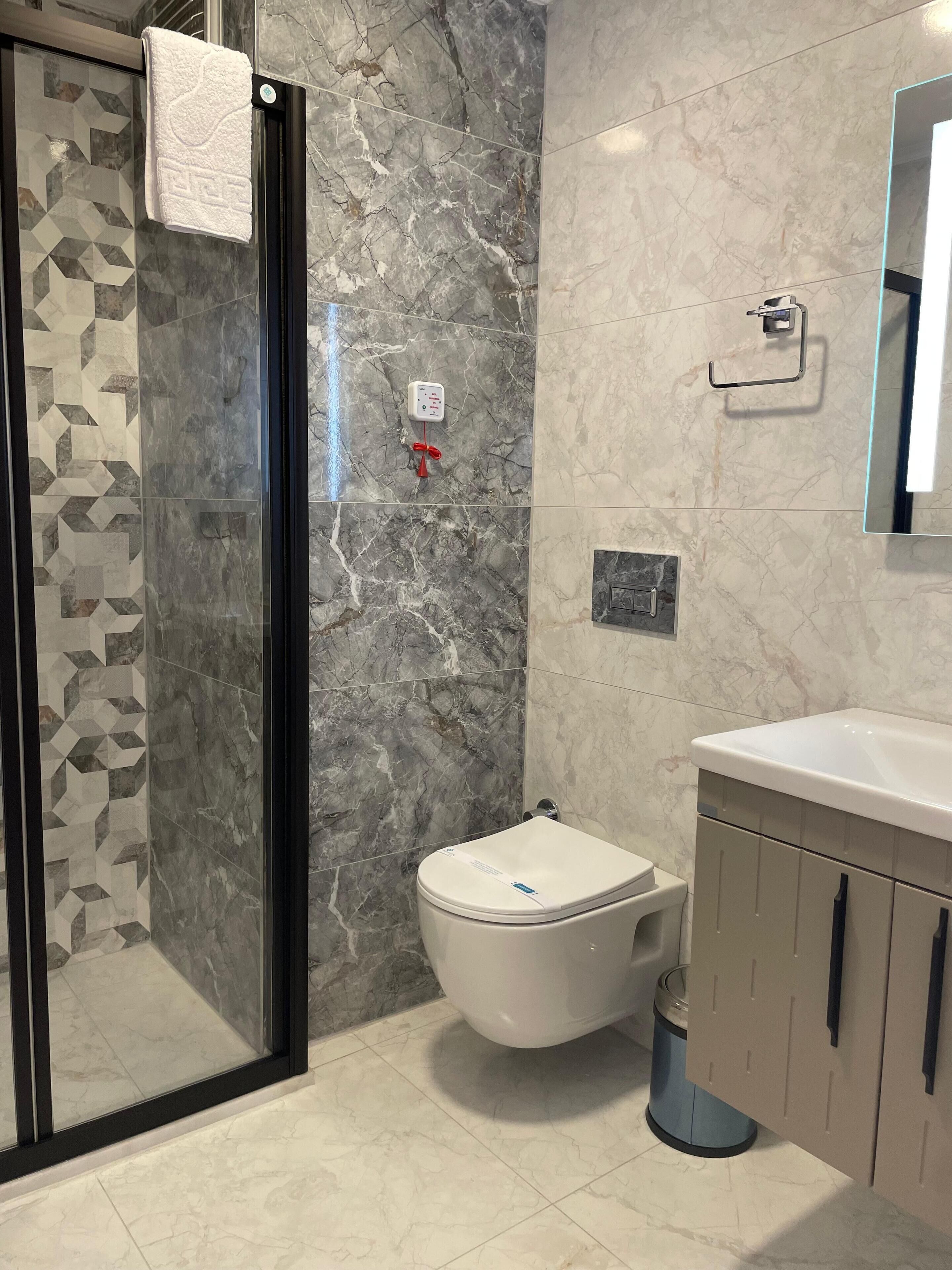 A bathroom with a glass shower enclosure, a toilet, and a sink with cabinets.