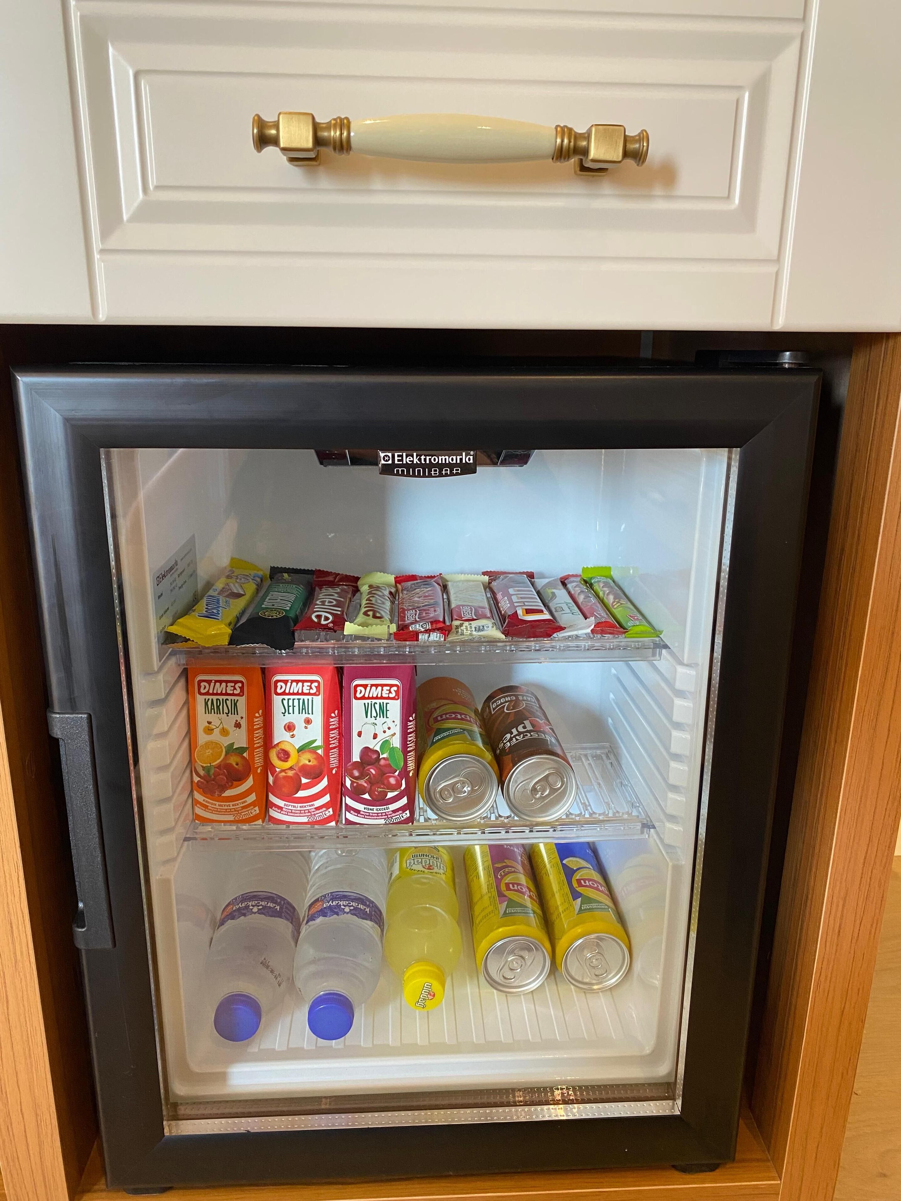 Un refrigerador pequeño con bebidas y aperitivos, incluyendo bebidas de la marca Dimes y agua embotellada.
