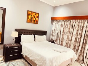Ein Hotelzimmer mit Bett, Nachttisch, Lampe, Spiegel und einem gemusterten Vorhang.