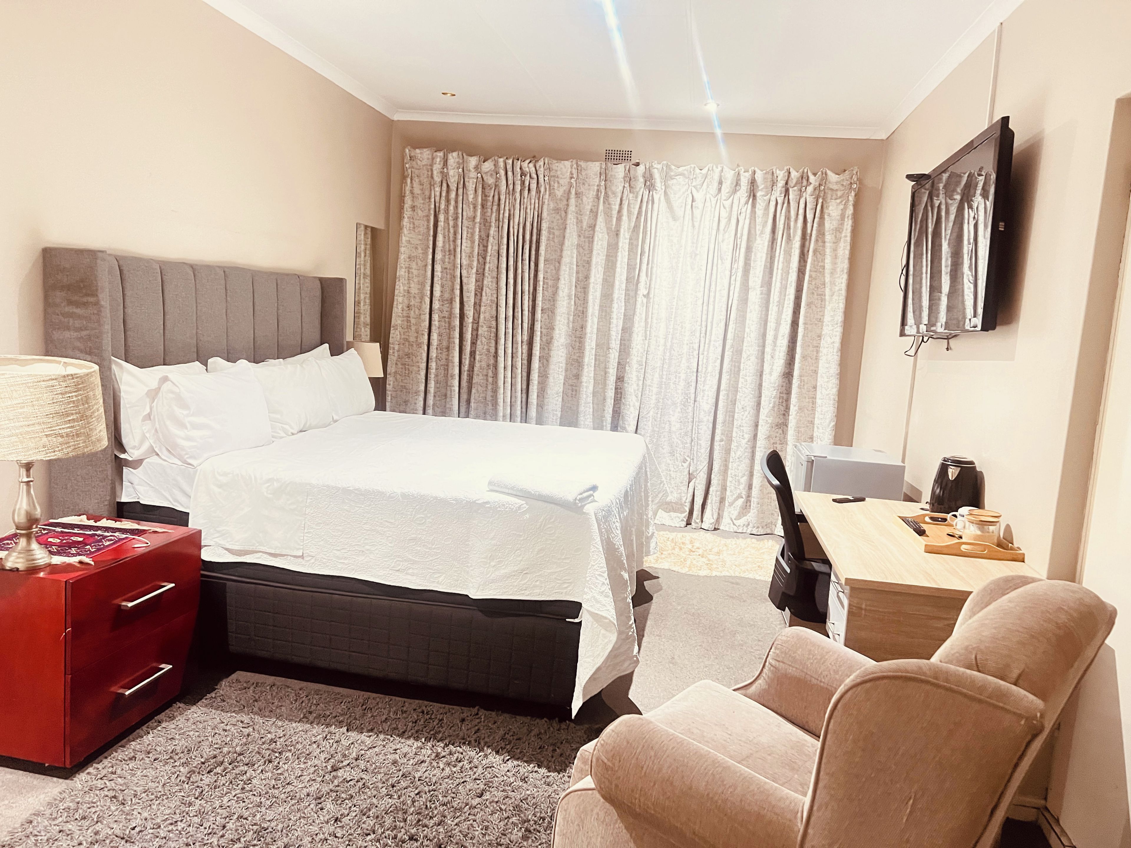Una habitación de hotel con cama, escritorio, silla, televisor y cómoda roja.