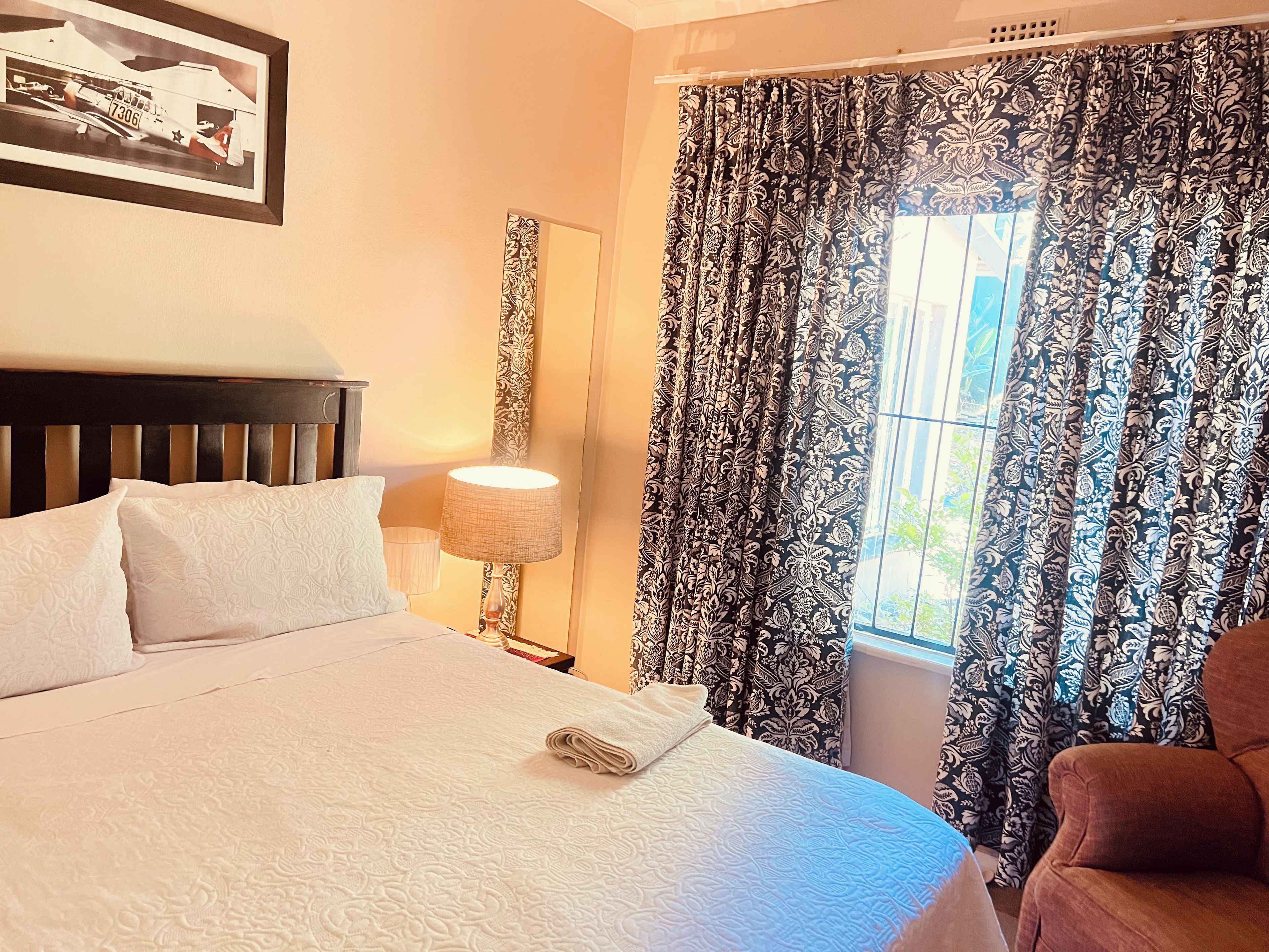 A hotel room with a bed, a nightstand, a lamp, curtains, and a framed picture on the wall.