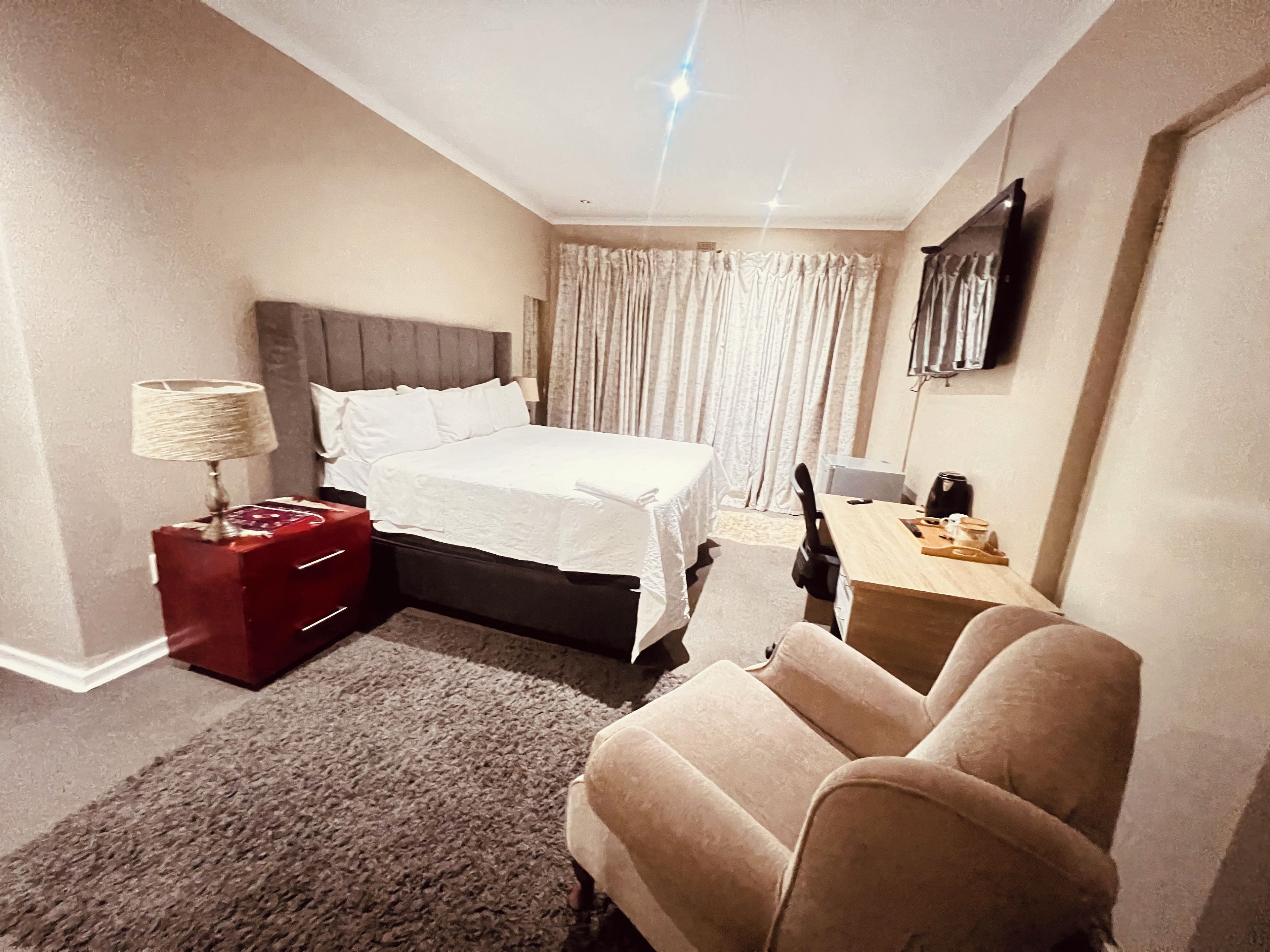 A hotel room with a bed, a desk, a chair, a lamp, and a television.