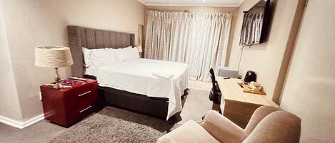 A hotel room with a bed, a desk, a chair, a lamp, and a television.