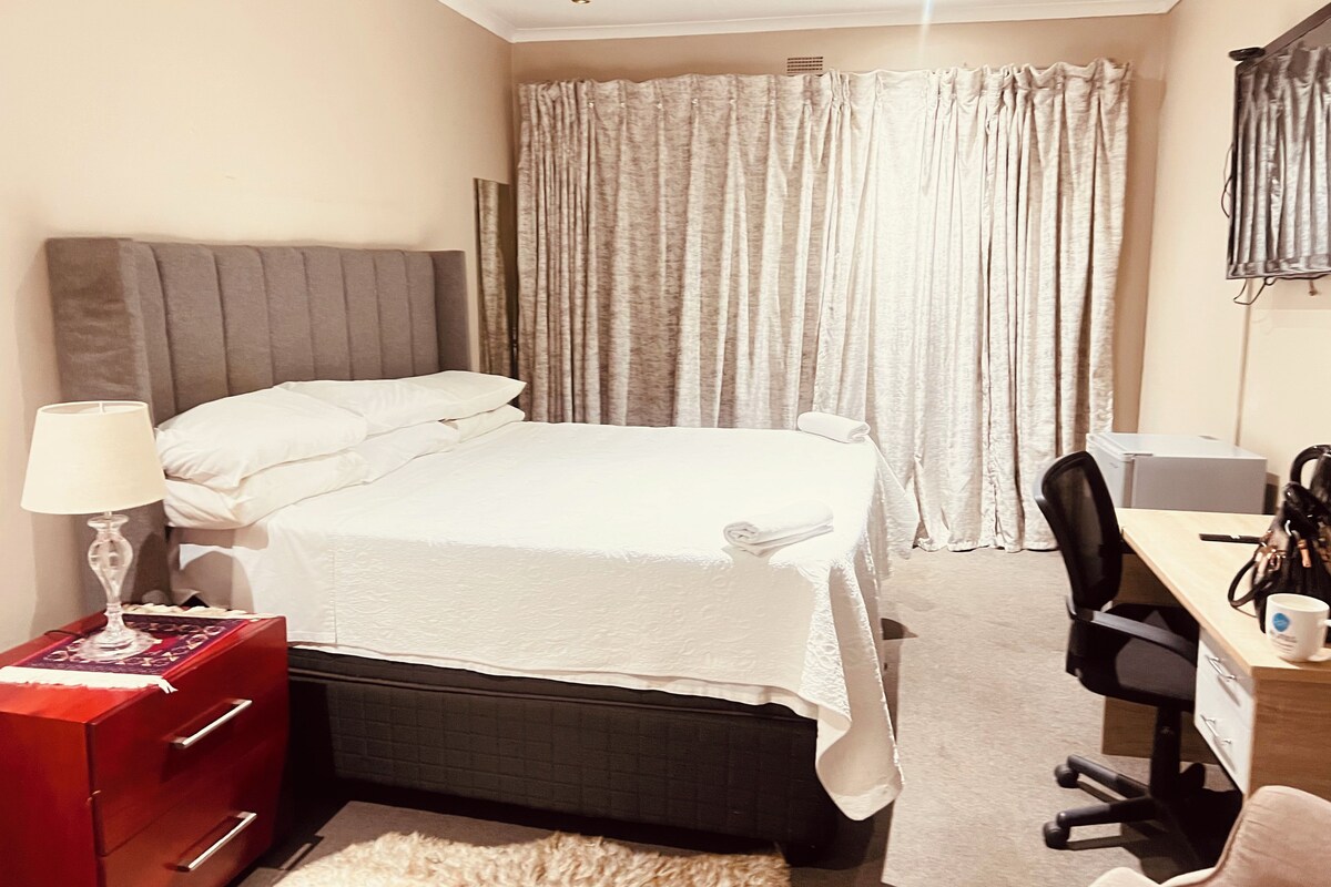 Habitación de hotel con cama, escritorio, silla, lámpara y cómoda roja.