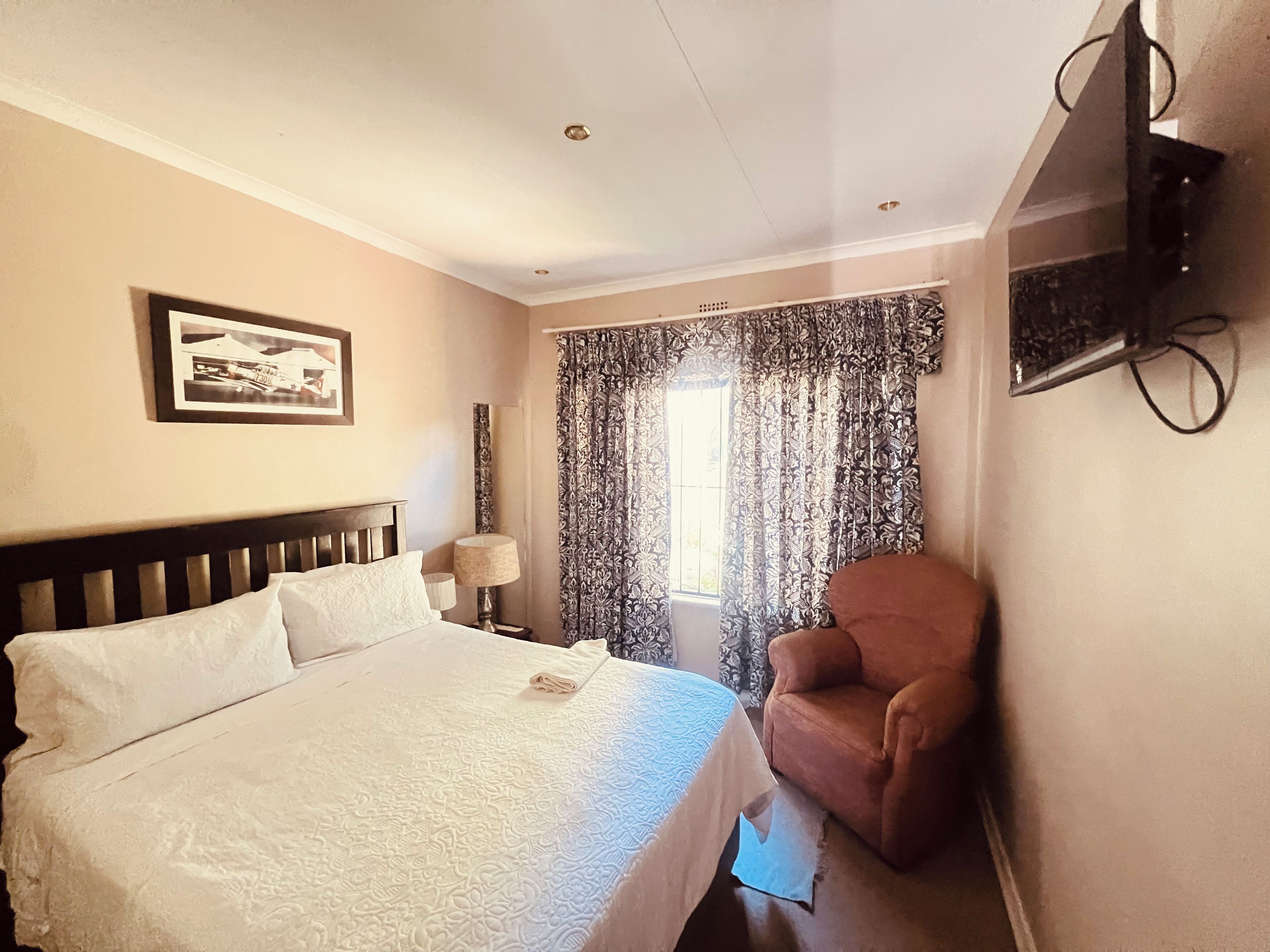 Ein Hotelzimmer mit Bett, Sessel, Wandfernseher und einem Vorhangfenster.