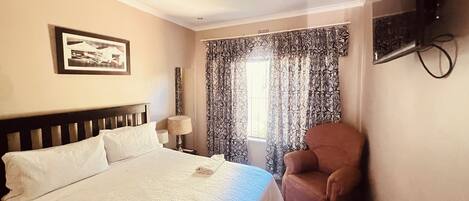 A hotel room with a bed, a chair, a television mounted on the wall, and a window with curtains.