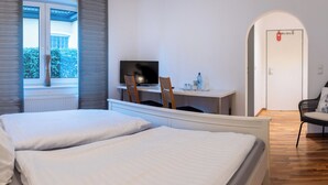Een hotelkamer met twee bedden, een bureau met een televisie, een stoel en een klein tafeltje met spullen erop.