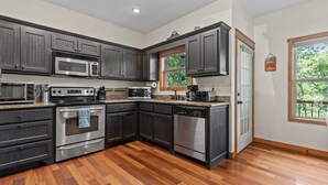 A modern kitchen with dark cabinetry, stainless steel appliances, and a wooden floor.