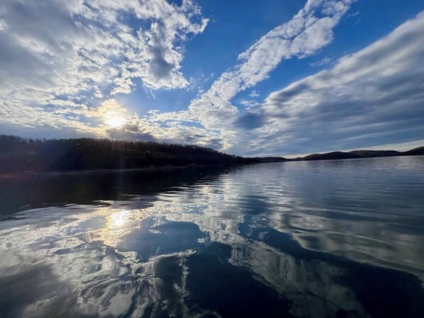 A calm lake with a clear reflection of the sky and clouds, surrounded by a forested landscape. - Lake Front, Lake Access, Surrounded by Fall Colors (Eureka Springs)
