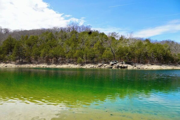 Una vista despejada de un lago con orilla arenosa y una colina boscosa al fondo.