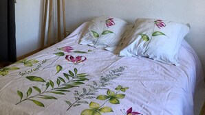 A bedroom with a floral bedspread, a round mirror on the wall, and a floor lamp.