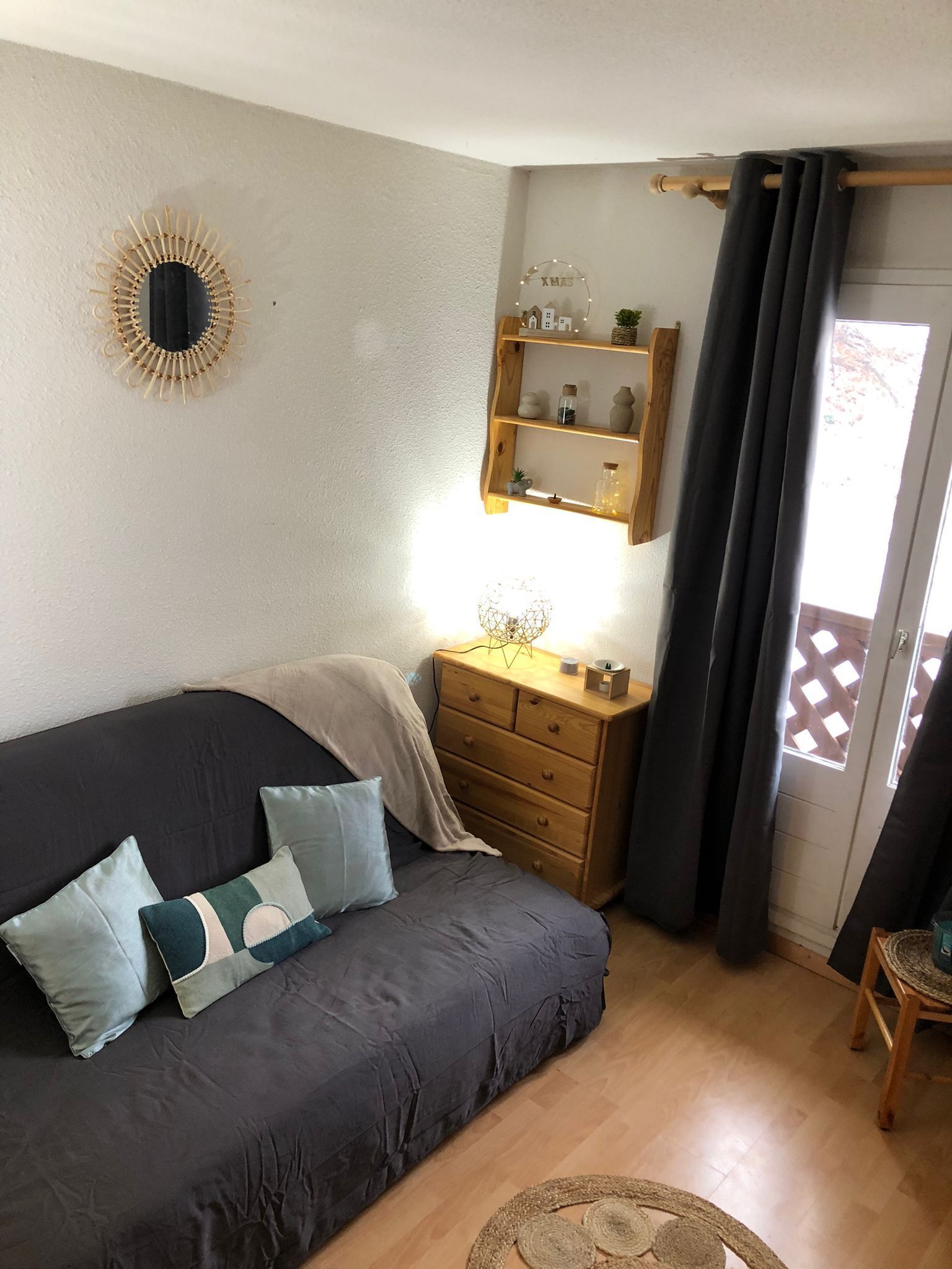 A cozy room with a dark-colored sofa, a wooden dresser, and a wall-mounted shelf with decorative items.
