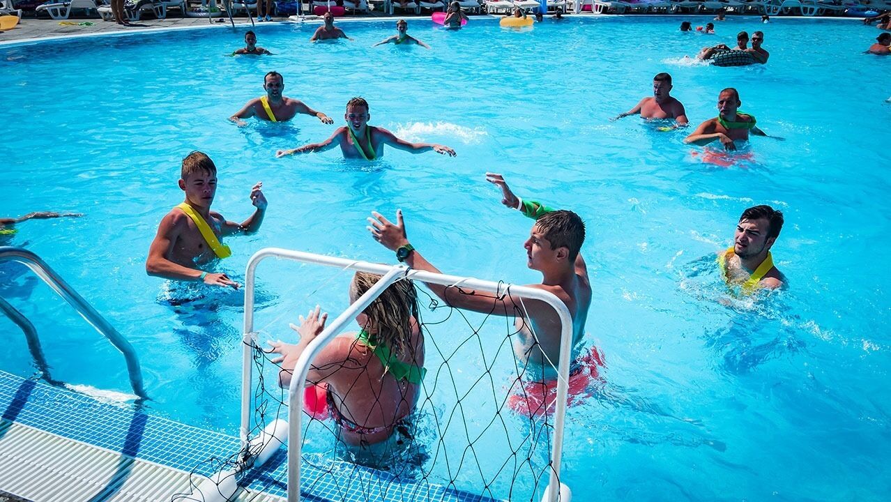 A swimming pool with people in the water, a pool ladder, and a safety net.
