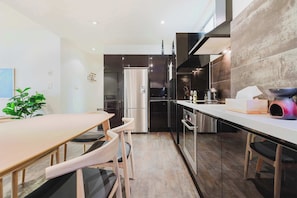 A modern kitchen with a stainless steel refrigerator, a dining area with a wooden table and chairs, and a large window providing natural light.