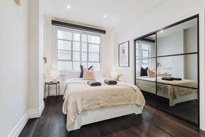 A bedroom with a large bed, a bedside table, a lamp, and a window.