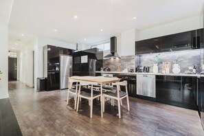 A modern kitchen with dark cabinetry, stainless steel appliances, and a wooden dining table with chairs.