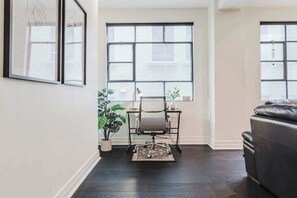A modern living room with a dark wood floor, a leather sofa, a desk with a chair, and a large window with a view.