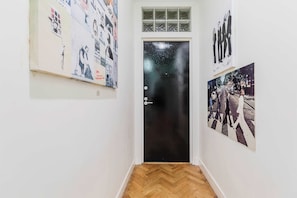 A hallway with a black door, wooden flooring, and wall-mounted artwork.
