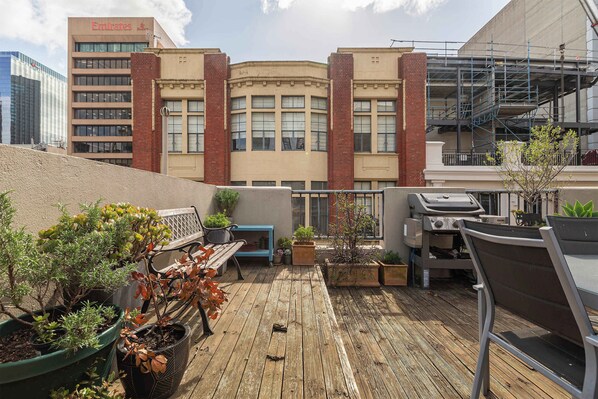 A rooftop patio with potted plants, a grill, and a seating area.