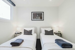 A hotel room with two beds, a framed picture on the wall, bedside lamps, and a window.