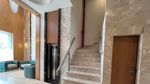 A modern lobby with a marble staircase, a wooden door, and green upholstered seating. - Esquire Hotel Mumbai (Mumbai)