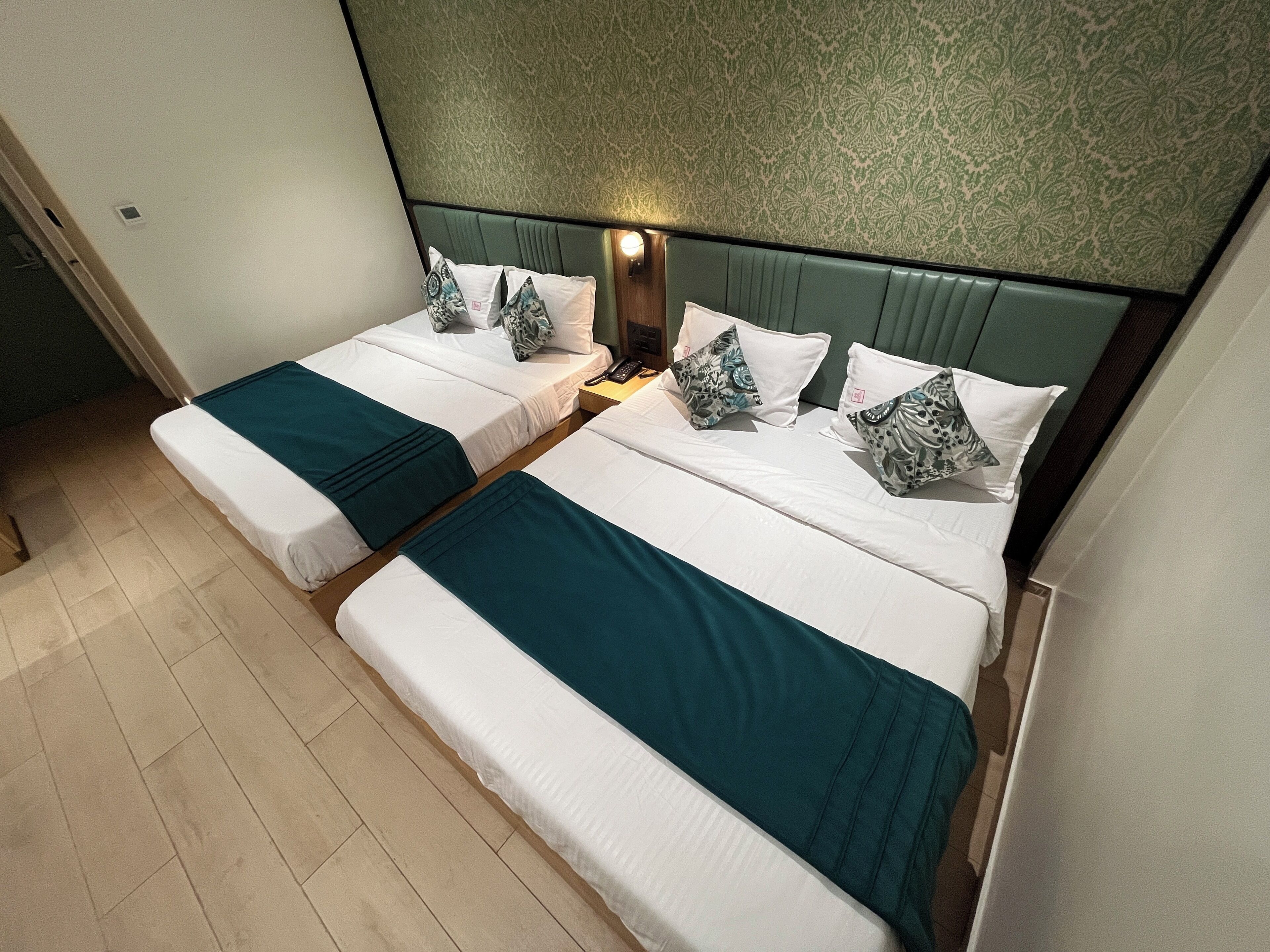 A hotel room with two single beds, each with a green bedspread and matching pillows.
